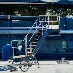 Square image of entrance to luxury yacht in Barcelona Yacht Port with parked bicycle near the stairs and pair of leather boots