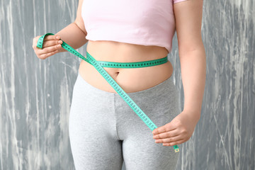 Overweight woman with measuring tape on grey background. Weight loss concept