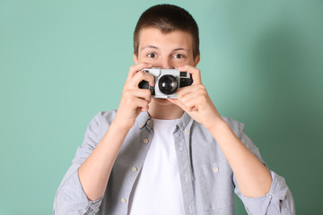 Teenage boy with photo camera on color background