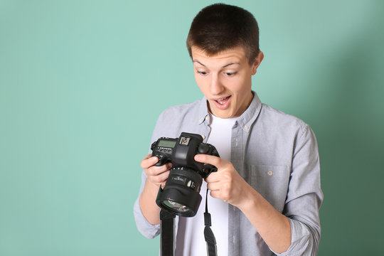 Surprised teenage boy with photo camera on color background