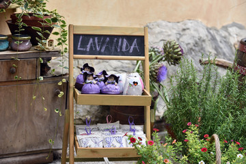 Homemade products made of lavander in purple color on a wooden pedestal, surrounded by green plants.