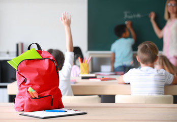 School backpack with stationery on table in classroom