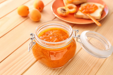 Jar of tasty apricot jam on wooden table