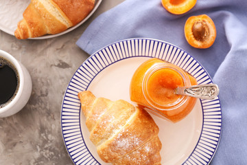 Plate with tasty apricot jam, croissants and coffee on grey table