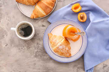 Jar with tasty apricot jam, croissants and coffee on grey table