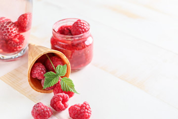 Fresh raspberries with wafer cone and jam in jar on white table