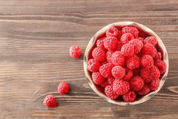 Bowl with fresh raspberries on wooden table