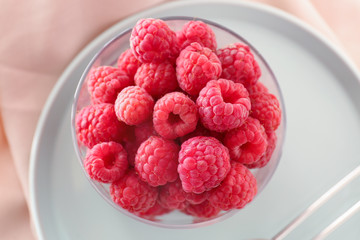 Glass with fresh raspberries on plate, closeup