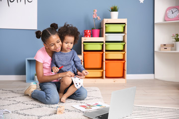 Cute African-American sisters with laptop watching cartoons at home