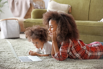 Cute African-American sisters with laptop watching cartoons at home