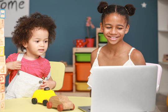 Cute African-American sisters with laptop watching cartoons at home