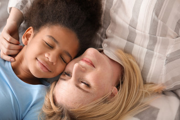 Happy woman with her African-American daughter lying on bed