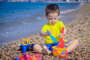 The boy plays on the beach in the toys for the sand. Children's games. Games on the beach. Galichny beach. Children's toys for sand. The baby is playing