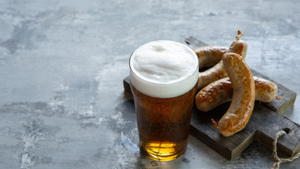 Glass of beer with foam on top on white stone background. Cold alcohol drink and sausages are prepared for a big friend's party. Concept of drinks, fun, food, celebrating, meeting, oktoberfest.