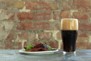 Glass of dark beer on the stone table and brick's background. Cold drink and meat snacks are prepared for a big friend's party. Concept of drinks, fun, food, celebrating, meeting, oktoberfest.