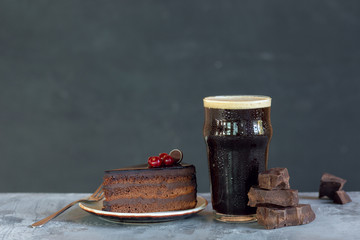 Glass of dark beer on the stone table and grey background. Cold drink and truffles with cake are prepared for a big friend's party. Concept of drinks, fun, food, celebrating, meeting, oktoberfest.