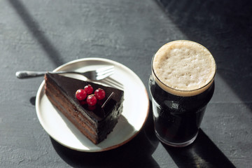 Glass of dark beer on the stone table background. Cold drink and cake or sweets are prepared for a big friend's party. Concept of drinks, fun, food, celebrating, meeting, oktoberfest.