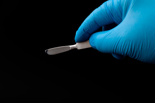 Surgical instruments in operating room and doctor performing surgery concept theme with a surgeon hand wearing blue latex gloves and holding a scalpel isolated on white background