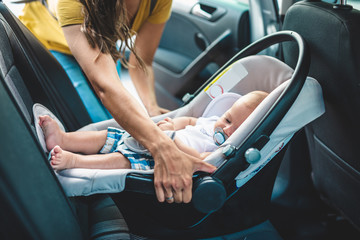 Young mother putting her baby boy on a safety child car seat.