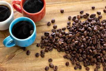 Three colorful cups of coffee on rustic wooden table near coffee beans top view