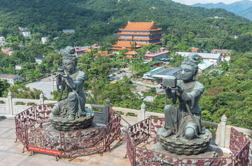 Buddhist statue praising and making offerings to the Tian Tan Buddha with Po Lin Monastery at background in Lantau island, Hong Kong