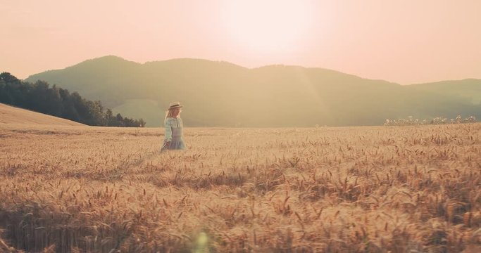 Beautiful woman walking in wheat field, sunset sun rays, Slow motion 4K.
