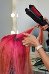 Hairdresser makes hairstyle to client using crimping irons. Hairdressing services. Girl with...