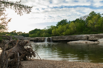 Waterfall at McKinney Falls State Park with large trees and blue sky background, Austin, Texas 