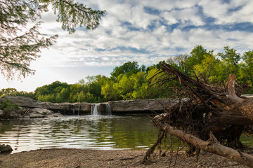 Fototapeta na wymiar Waterfall at McKinney Falls State Park with large trees and blue sky background, Austin, Texas 