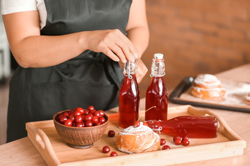 Woman with tasty cherry juice and sweet bun on tray at table
