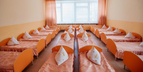 Beds and cots in brightly colored dormitory of a nursery.A lot of children's cots - obrazy, fototapety, plakaty