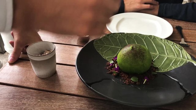 Waiter breaking sphere dessert cooked with lucuma ice cream, smoked cacao, carob and chocolate with spices.