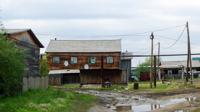Wooden apartment house Barak stands behind a fence at the end of the street with a puddle under the fat sky in the village of ulus Yakutia Suntar.