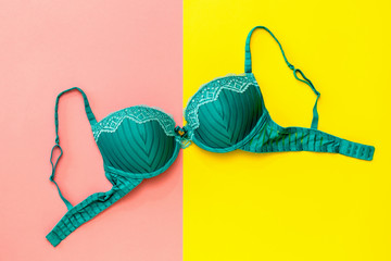 Green female bra on yellow and pink background. Flat lay. - obrazy, fototapety, plakaty