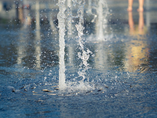 Dry fountain on town square, close up view. Water stream splashing on fountain coating with many drops. Kids bare feet near fountain. Selective soft focus. Blurred background
