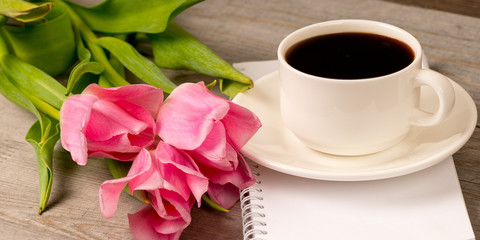 morning coffee in white porcelain cup and spring pink tulips bouquet over rustic wooden table