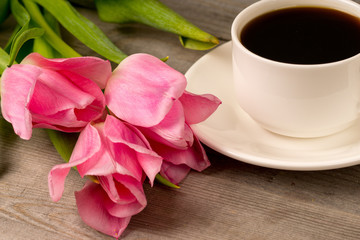 morning coffee in white porcelain cup and spring pink tulips bouquet over rustic wooden table
