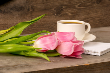 morning coffee in white porcelain cup and spring pink tulips bouquet over rustic wooden table