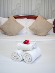 White clean towels decoration with red flower on white clean bed in hotel room.