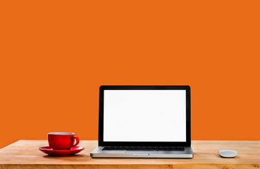 Workplace with notebook laptop and coffee cup comfortable work a wooden table on orange background.