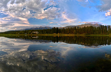 Fototapeta na wymiar Panoramic view Columbia Lake. Beautiful reflections of mountains, trees and a vacation cottage in calm lake in the morning. Columbia lake. British Columbia. Canada