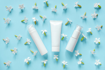 White flowers and three cosmetic, medical white tube, bottle for cream, ointment, toothpaste or other product on blue background. Concept natural organic cosmetics, homeopathic cosmetology Mockup