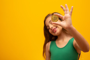 Child holding cryptocurrency in metal. Gold coin. Golden. On yellow background.