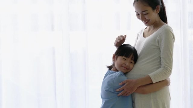 Asian family daughter hug and listening sound flex in pregnant mother belly. Children flex in the stomach. Concept of family, hope and new born.
