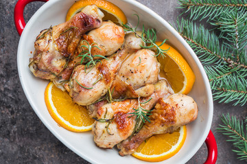 Baked chicken drumstick in a dish with orange and rosemary, top view