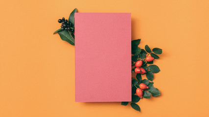 Party invitation letter. Pink mockup paper sheet with rose hip decoration on orange background. Copy space.