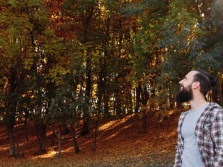 Fall landscape. Portrait of happy male tourist enjoying time in nature park. Blur trees and fallen leaves background.