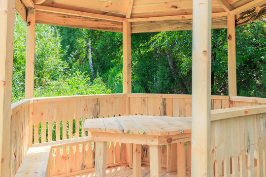 Wood products, bower. Carpentry skill. Camping, a shelter for tourists. New arbor, gazebo made of wood and a table against the backdrop of summer wood for relaxing and dining in the yard outdoors