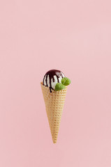 Delicious white ice cream scoop in crisp waffle cone decorated chocolate sauce,  mint leaf on pink background, vertical.