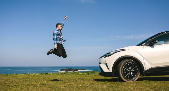Young man jumping happy in front of a car outdoors